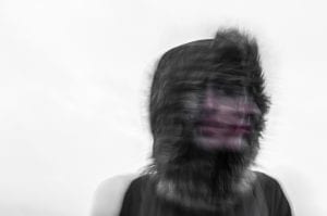 Blurred image of woman wearing a fur-lined hood shaking her head; image by Ehimetalor Unuabona, via unsplash.com.