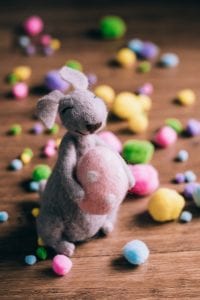 Stuffed rabbit holding a stuffed Easter egg surrounded by colored cotton balls; image by freestocks.org, via Unsplash.com.