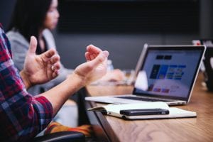 People sitting around a table with laptop and cell phone having a meeting; image by Headway, via unsplash.com.