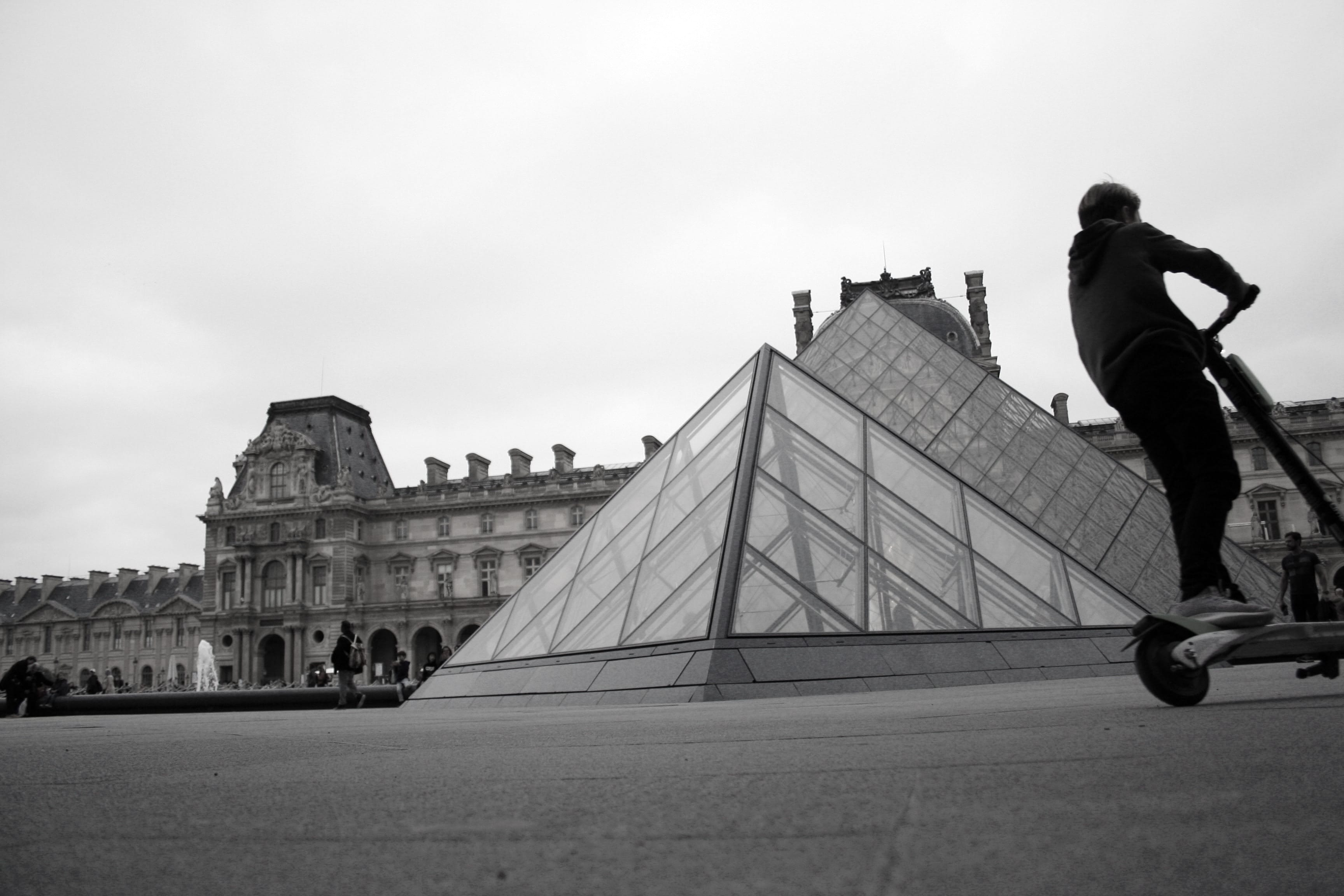 Man riding a Lime electric scooter outside the Louvre in Paris, France; image by Timothy K, via unsplash.com.