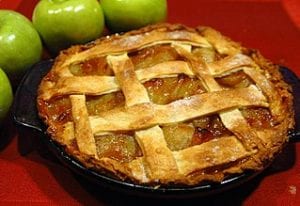 A golden brown lattice-crusted apple pie, with four green apples sitting nearby.