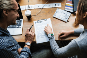 A man and a woman reviewing a contract at a desk; image by Rawpixel, via Unsplash.com.