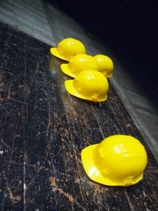 Five yellow hardhats on a wooden surface; image by Silvia Brazzoduro, via Unsplash.com.
