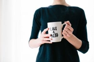 Woman in black blouse holding a white coffee mug that reads “Like a Boss;” image by Brooke Lark, via Unsplash.com.