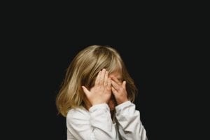 Young girl covering her face with both hands; image by Caleb Woods, via Unsplash.com.