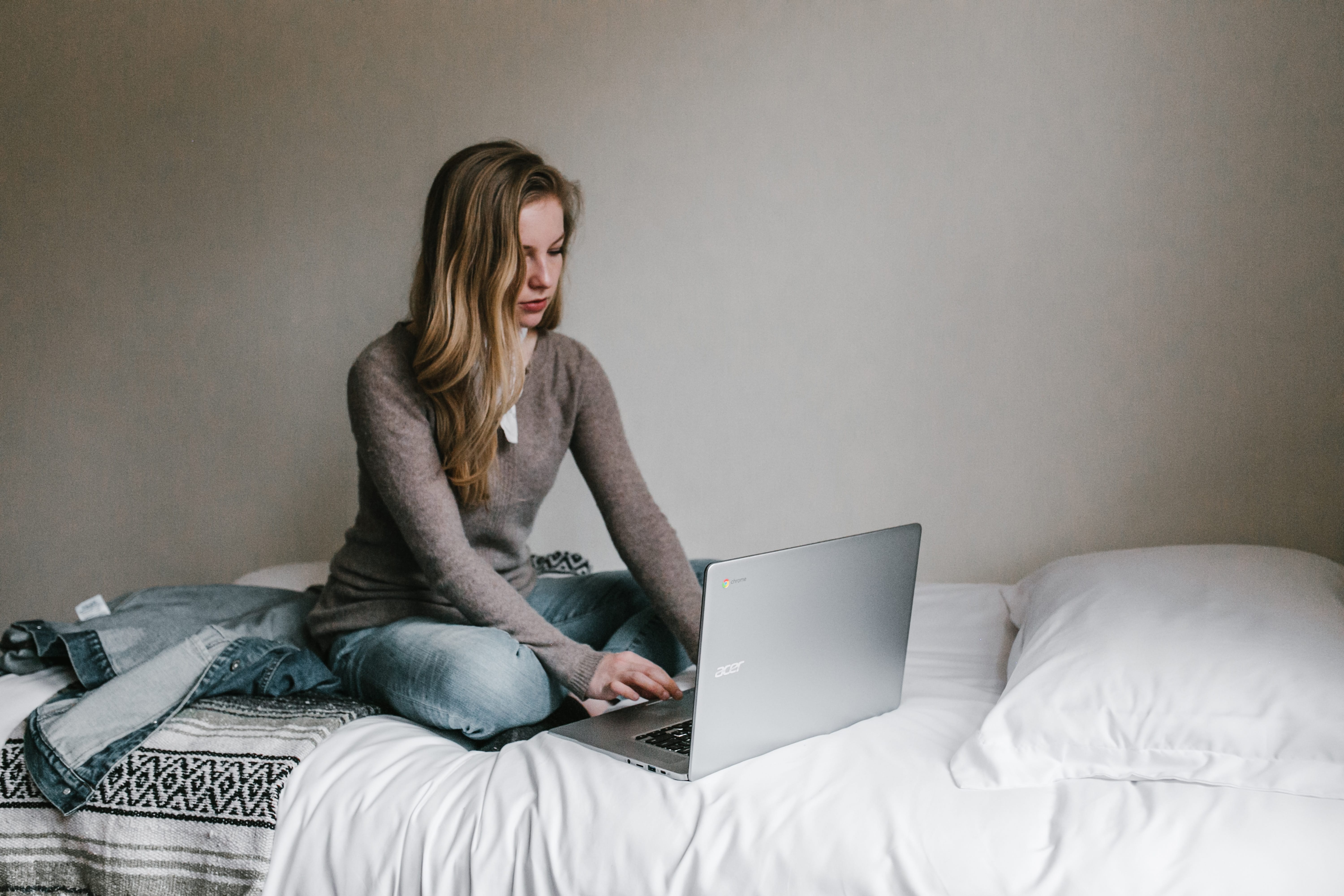 Woman sitting on bed working on laptop; image by Andrew Neel, via Unsplash.com.