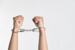 Person’s forearms raised to the sky, wearing handcuffs; image by niu niu, via Unsplash.com.