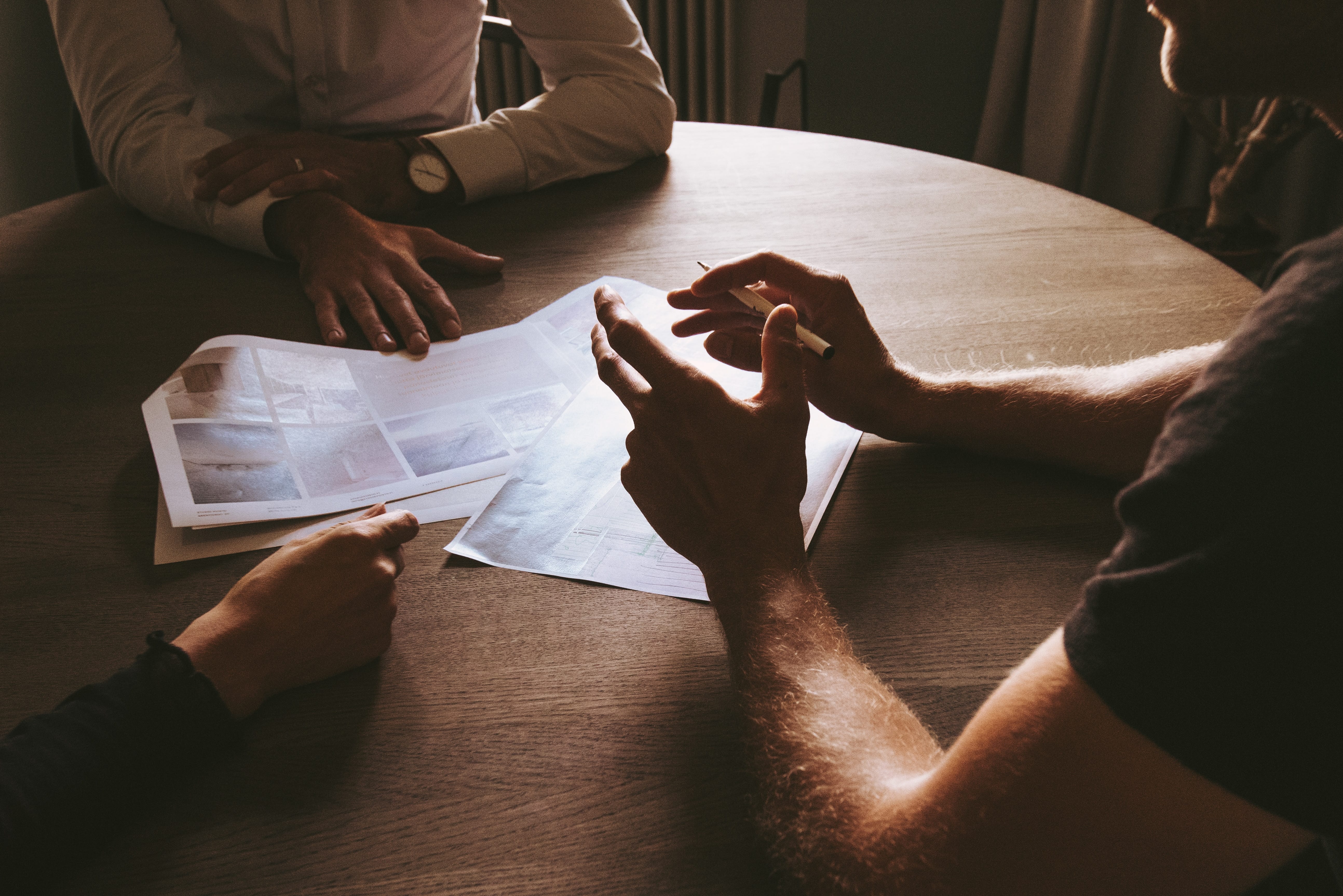 Three men sitting around a brown wooden table; image by Thomas Drouault, via Unsplash.com.