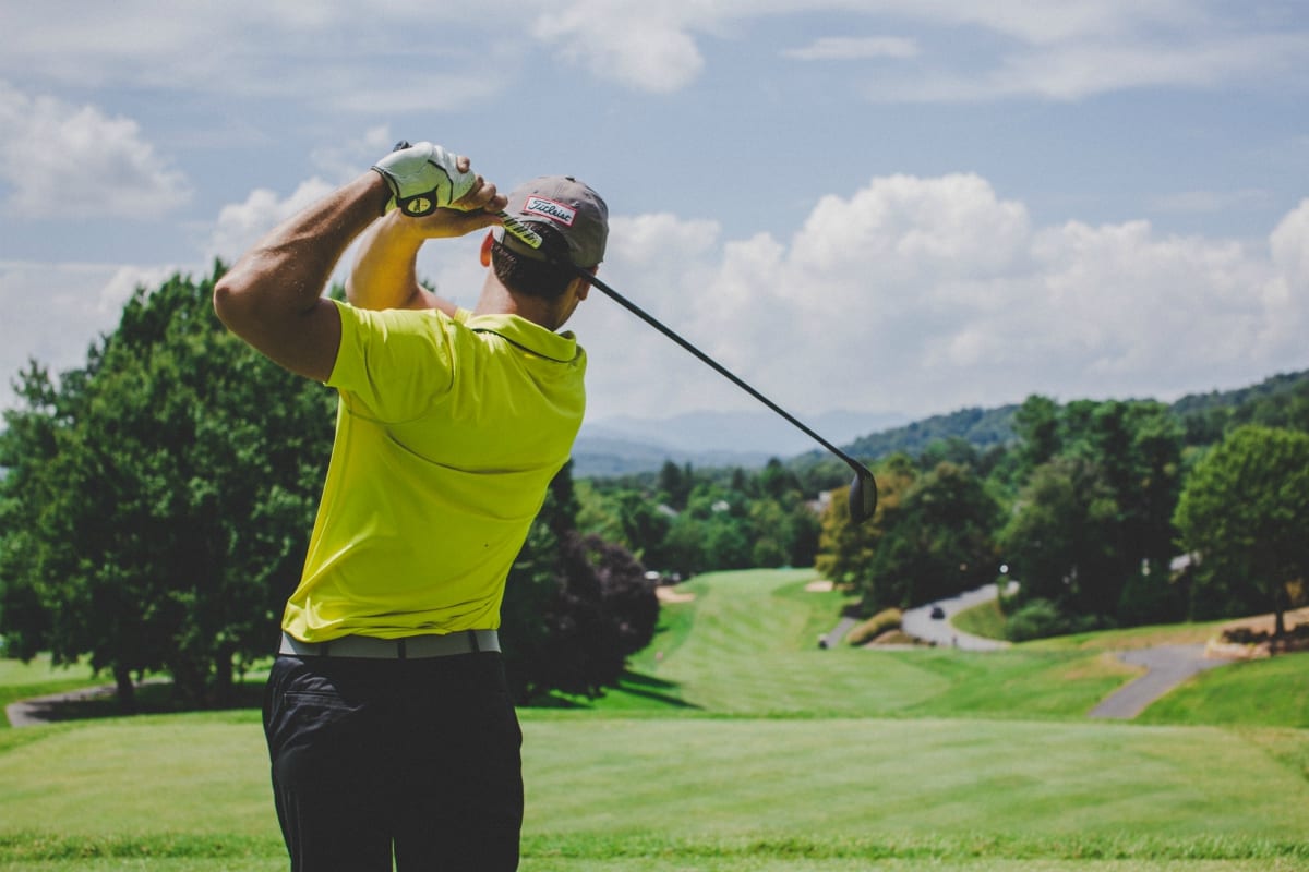 Man in bright yellow shirt finishing golf swing on golf course; image by Court Prather, via Unsplash.com.