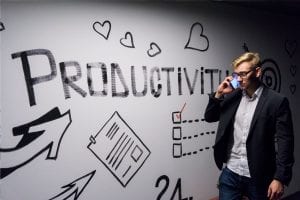 Man holding smartphone looking at whiteboard about productivity; image by Andreas Klassen, via Unsplash.com.