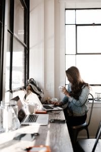 Woman seated at a long table working on a laptop; image by Andrew Neel, via Unsplash.com.