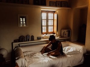 Man sitting on bed near open window; image by Joel Overbeck, via Unsplash.com.