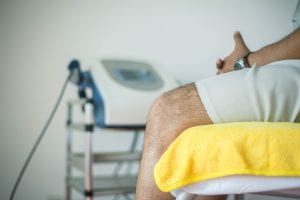 Man in white shorts sitting on yellow sheet on examination table, equipment in background; image by Marlon Lara, via Unsplash.com.