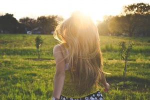 Blonde woman in grassy field facing sunshine; image by Morgan Sessions, via Unsplash.com.