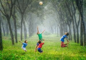 Four boys playing with a ball on a grassy forest path; image by Robert Collins, via Unsplash.com.