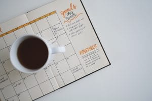 Cup of coffee resting on planner open to November, “Goals this month” written in right margin; image by Estée Janssens, via Unsplash.com.