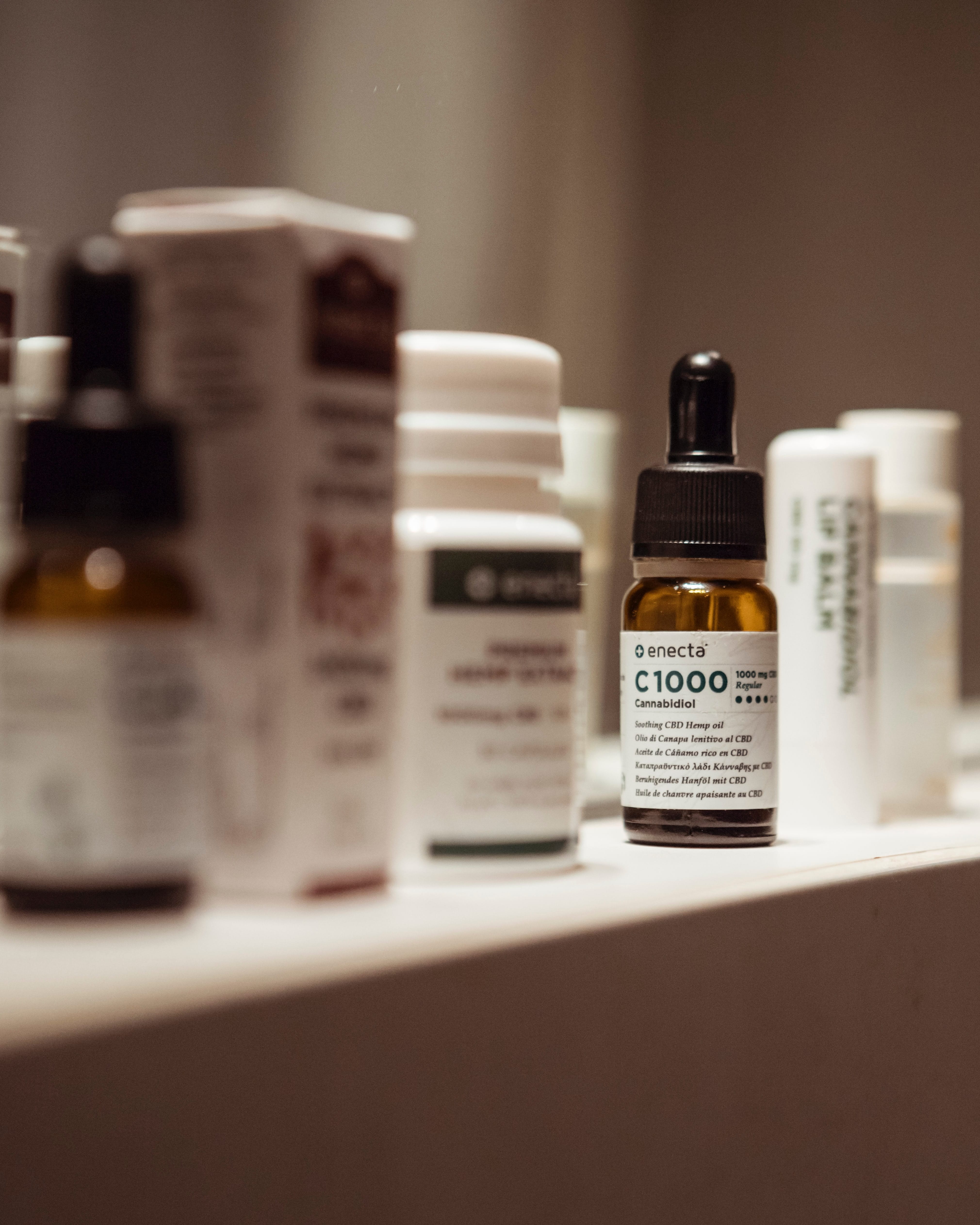 Shelf with bottles of medicine in soft focus and a bottle of CBD oil in clear focus; image by Francesco Mazzone, via Unsplash.com.