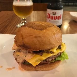 A cheeseburger in a bun on a wrapper, with a beer in the background.