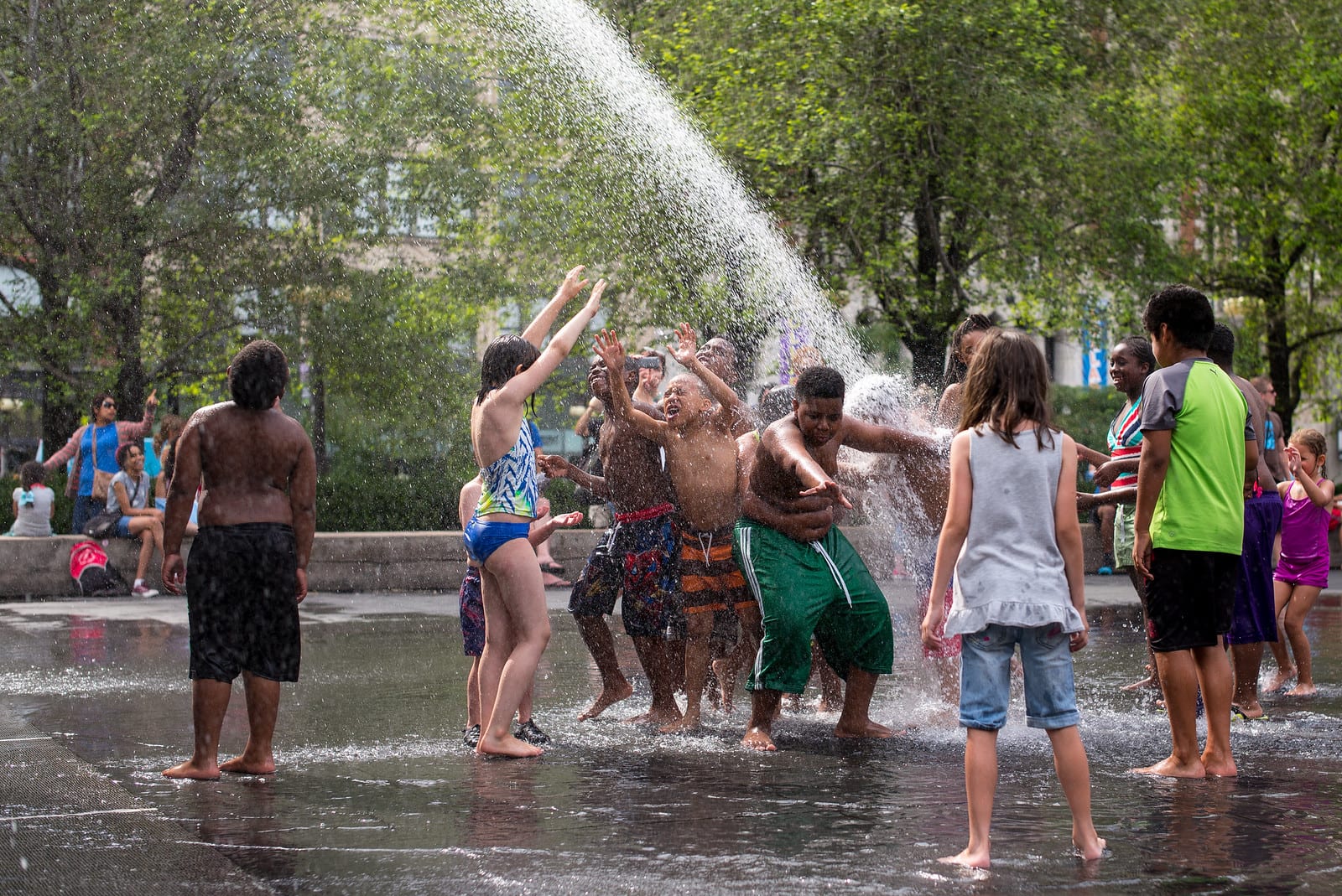 A diverse group of young people splashing around in a fountain in a Chicago park on a hot day.