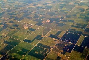 Grid squares of farmland in various shades of green, as seen from above the countryside.