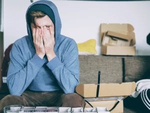 Man in hoodie holding his face in his hands; image by Christian Erfurt, via Unsplash.com.