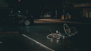 Bicycle on its side in the middle of a dark street with a car nearby; image by Ian Valerio, via Unsplash.com.