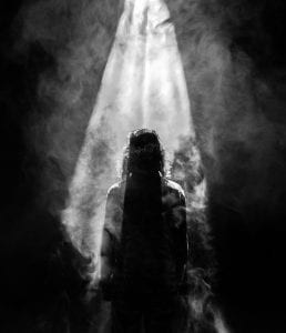 Person facing opposite in smoky spotlight; image by Mads Schmidt Rasmussen, via Unsplash.com.