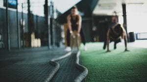One woman doing push-ups and another using battle ropes at the gym; image by Meghan Holmes, via Unsplash.com.