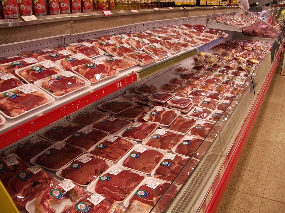 A grocery store meat display, with stacks of individually wrapped foam trays of meat in a refrigerated case.