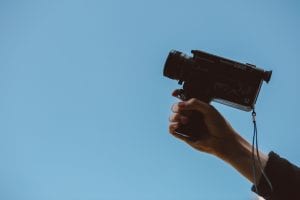 Person holding video camera; image by Thomas William, via Unsplash.com.