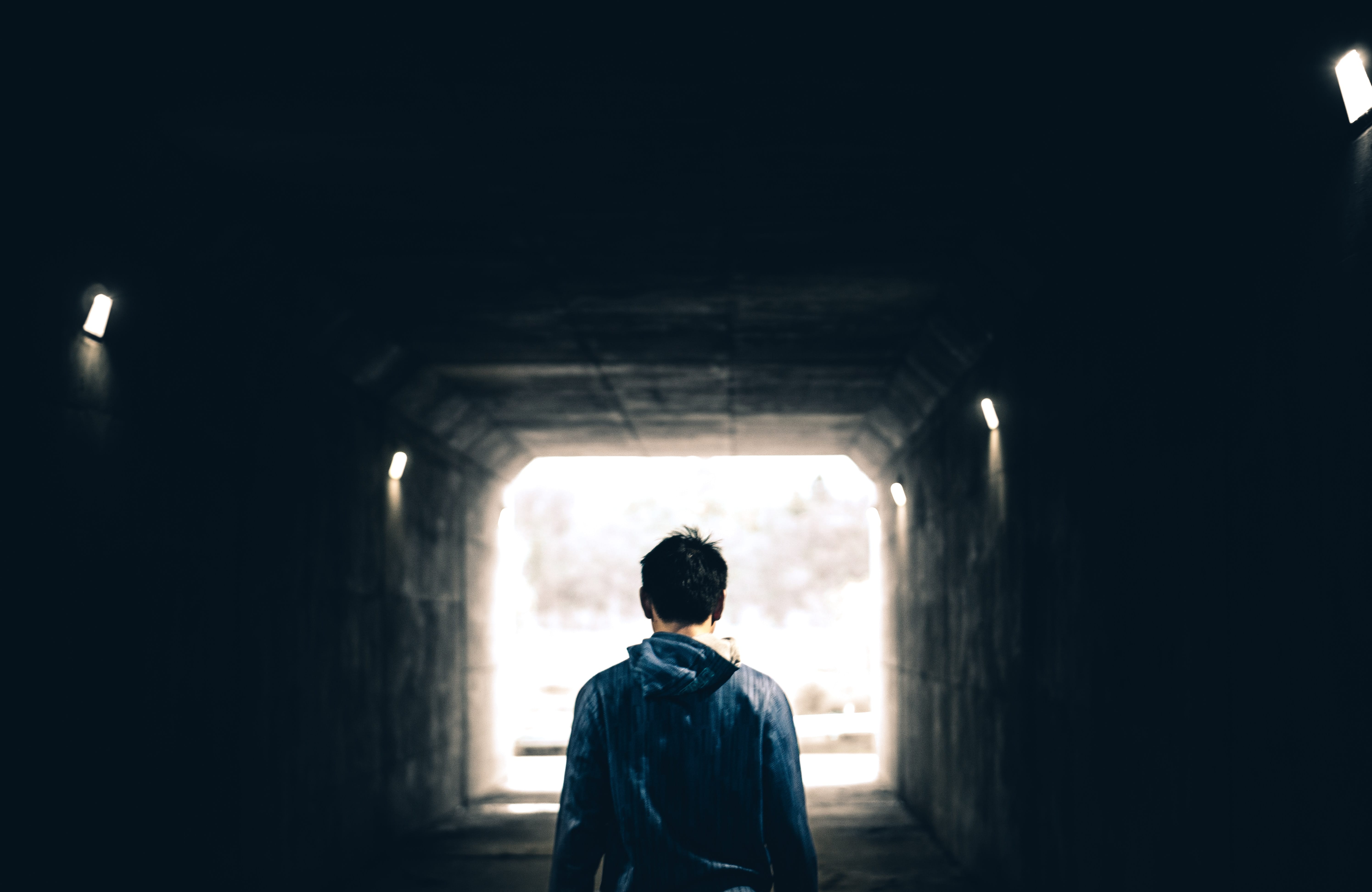 Man walking toward light at the end of a tunnel; image by Warren Wong, via Unsplash.com.