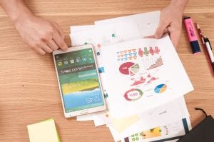 Man using tablet while reviewing financial papers; image by William Ivin, via Unsplash.com.