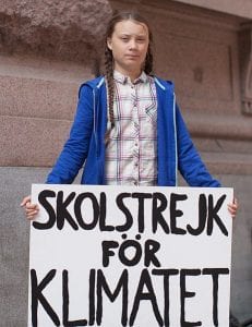 A young woman in braids with a blue jacket holds a sign.