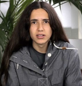 A young Native man wearing a grey zippered sweatshirt looks directly at the camera.