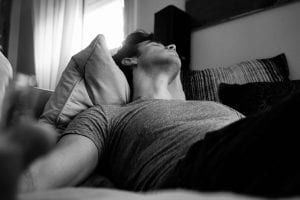 Black and white photo of man sleeping on sofa; image by Adi Goldstein, via Unsplash.com.