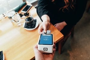 Person holding credit card swipe machine; image by Blake Wisz, via Unsplash.com.