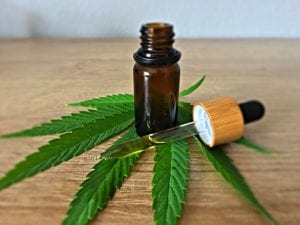 Brown glass bottle of oil with dropper, resting on marijuana leaf; image by CBD Infos, via Unsplash.com.