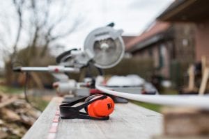 Red and black earmuffs next to miter saw; image by Cetteup, via Unsplash.com.