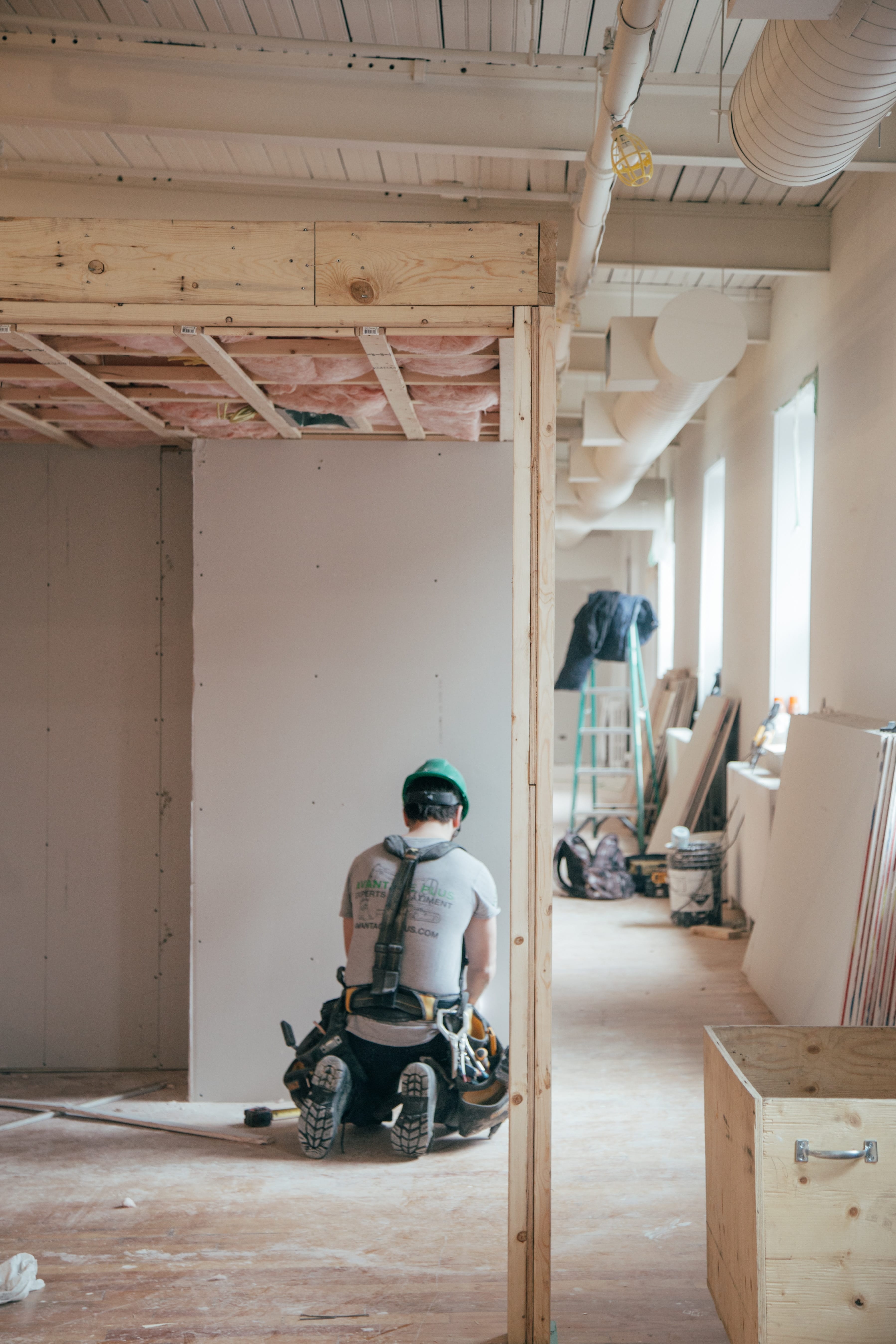 Construction worker kneeling in front of a wall; image by Charles, via Unsplash.com.