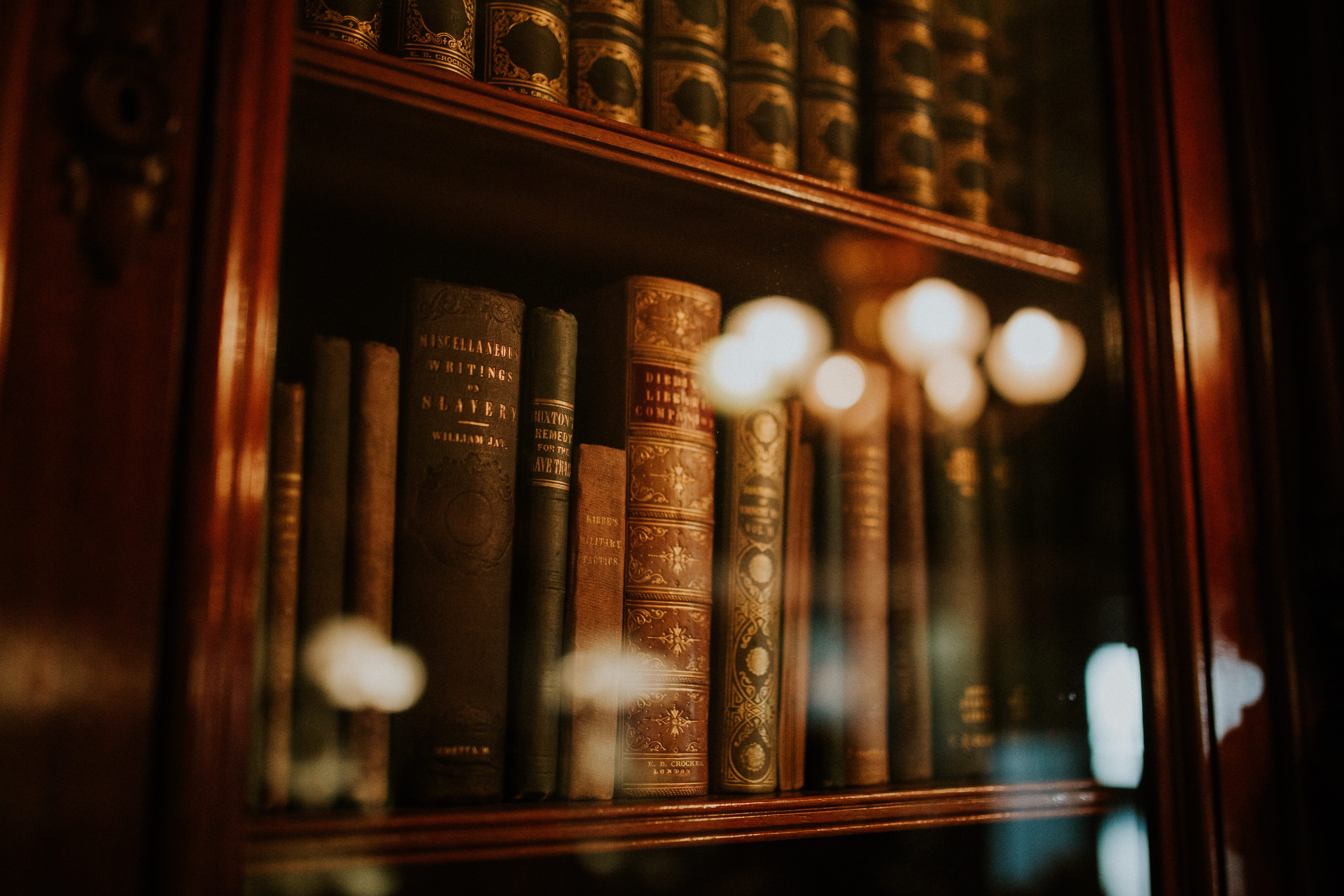 Wooden bookcase with glass door and old books; image by Clarisse Meyer, via Unsplash.com.