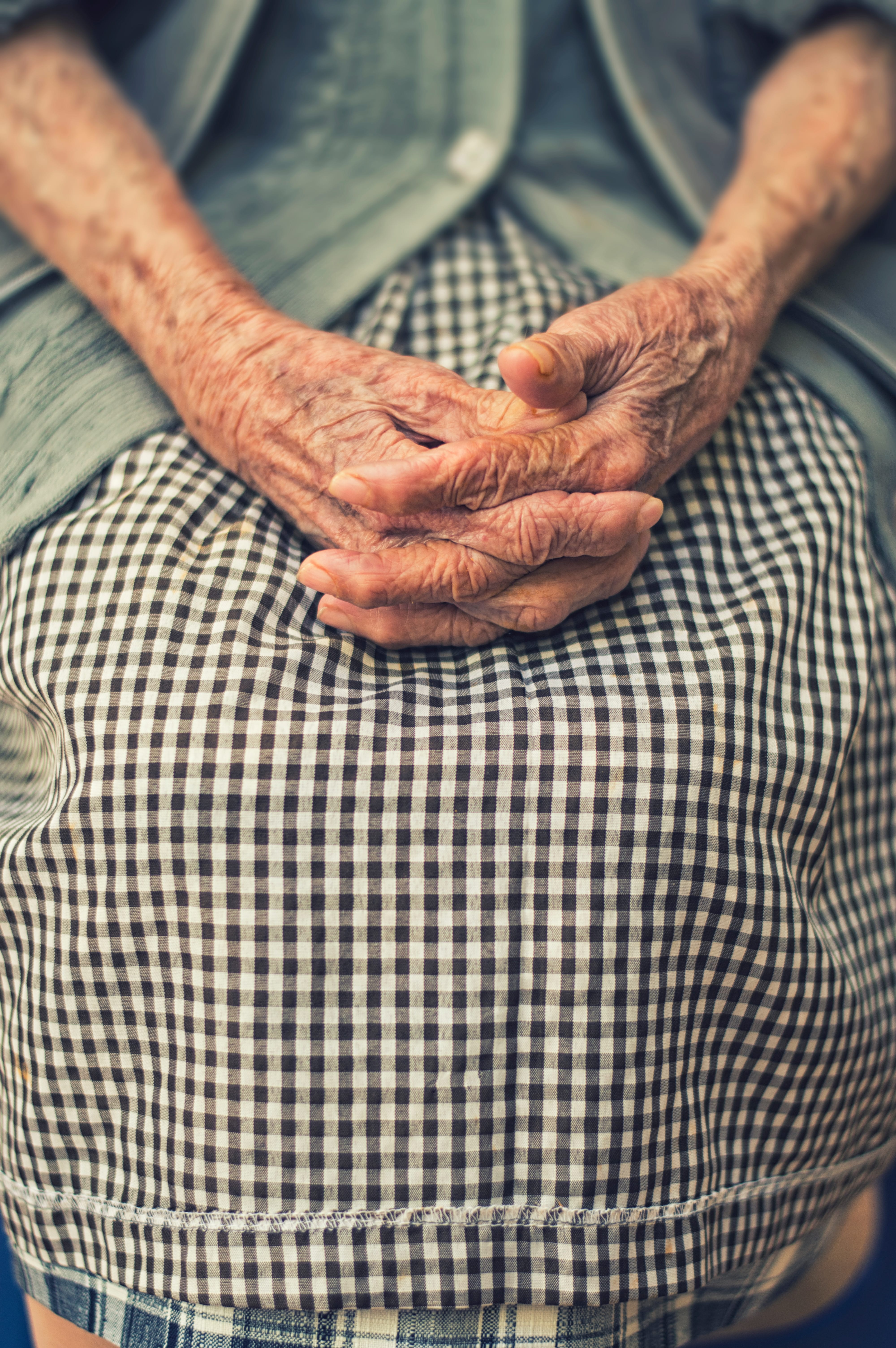 Elderly woman with hands folded in her lap; image by Cristian Newman, via Unsplash.com.