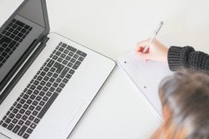 Woman with laptop taking notes on a notepad; image by J. Kelly Brito, via Unsplash.com.