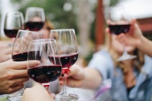 People toasting each other with glasses of red wine; image by Kelsey Knight, via Unsplash.com.