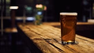 Glass of beer on wooden table; image by mnm.all, via Unsplash.com.