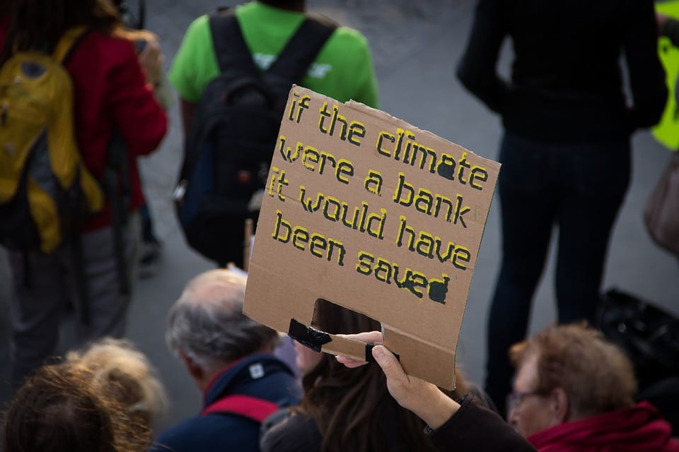 A protest march. One man holds a sign that says, "If the Climate Were a Bank, It Would Have Been Saved."
