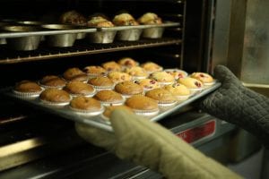 Person wearing oven mitts removing tray of muffins from oven; image by Taylor Grote, via Unsplash.com.