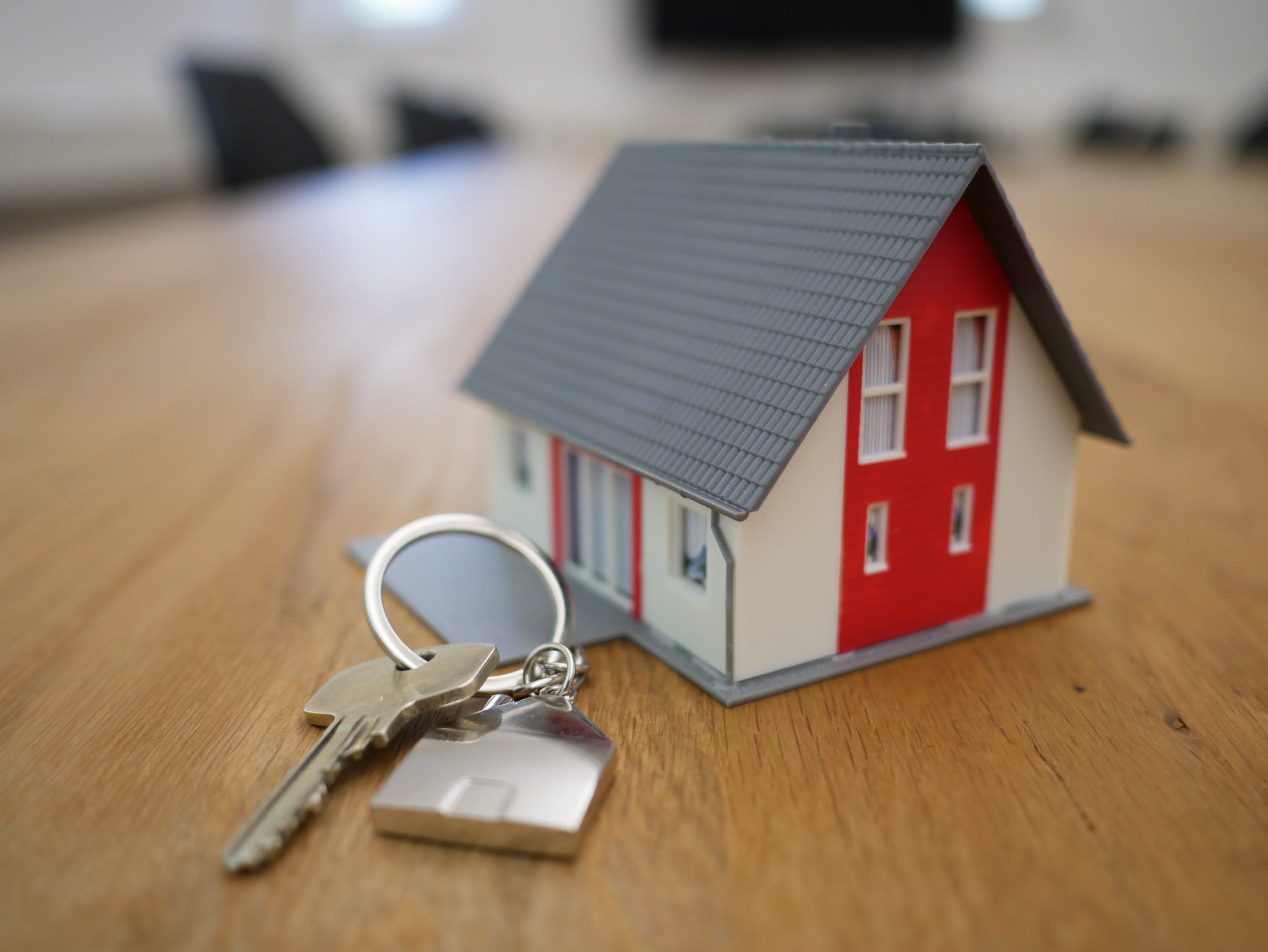 Red, white and grey toy house sitting on table next to house key on keyring shaped like a house; image by Tierra Mallorca, via Unsplash.com.