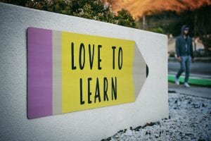 “Love to learn” pencil signage on wall near walking man; image by Tim Mossholder, via Unsplash.com.