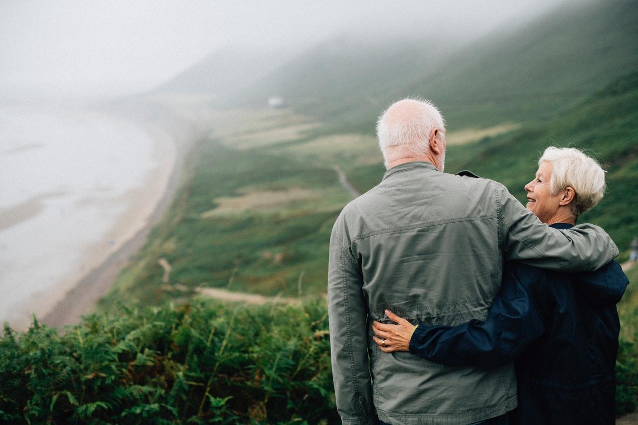 Older man and woman looking over a beach scene; image via Pexels.com.