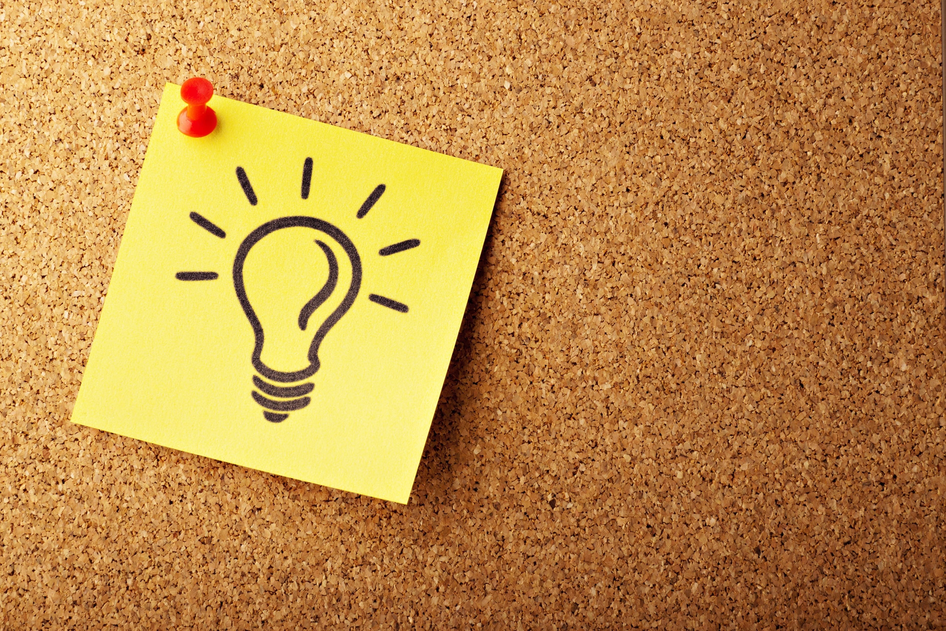 Yellow sticky note with a light bulb drawn on it tacked to a cork board; image by AbsolutVision, via Unsplash.com.